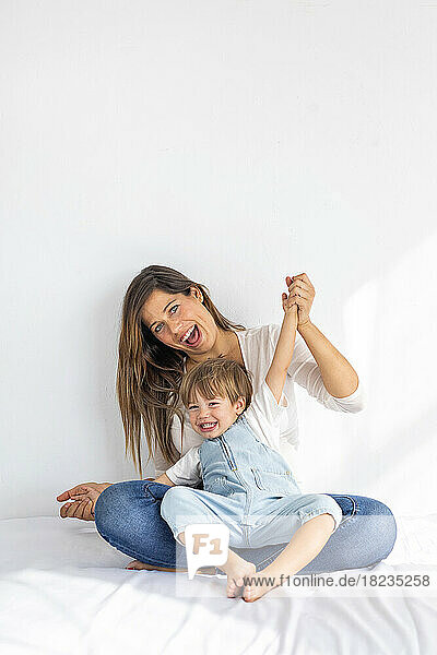 Happy woman and son having fun sitting on bed at home