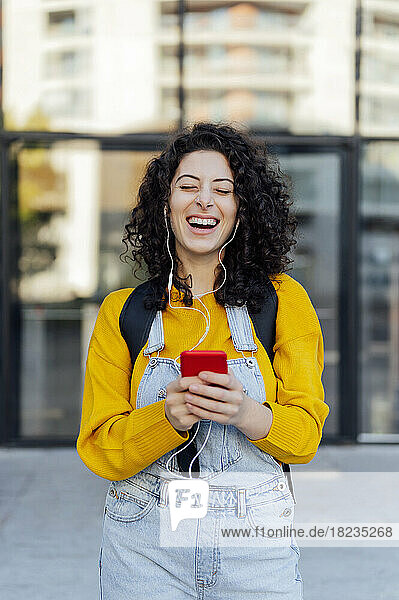 Happy young woman with mobile phone listening to music through in-ear headphones