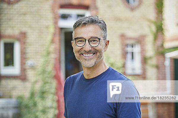 Smiling man wearing eyeglasses in front of house