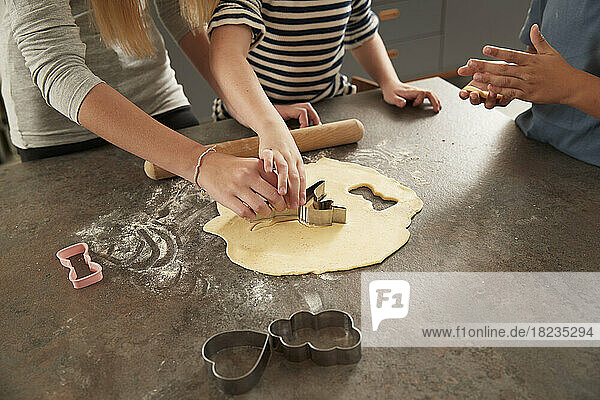 Hands of children using cookie cutter at kitchen counter