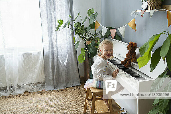 Glückliches Mädchen  das zu Hause auf einem Hocker am Klavier sitzt