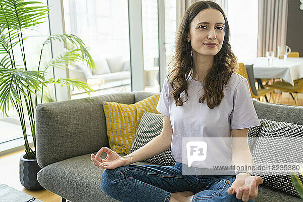 Lächelnde Frau meditiert auf dem Sofa im Wohnzimmer