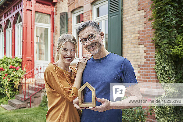 Smiling woman standing by man holding house model in garden