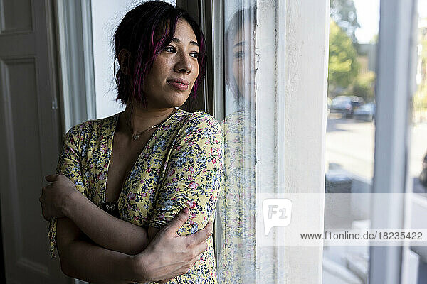 Smiling young woman looking through window at home