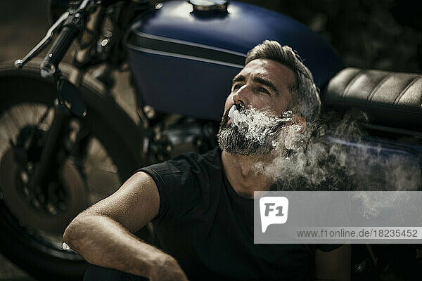 Man sitting by motorcycle and smoking cigarette