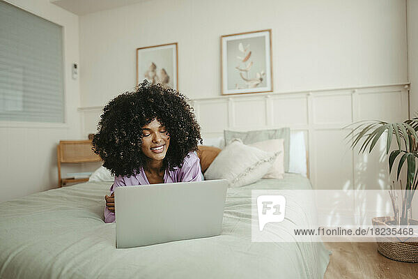Afro woman using laptop on bed at home