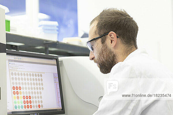 Scientist wearing glasses examining medical test results on computer in laboratory