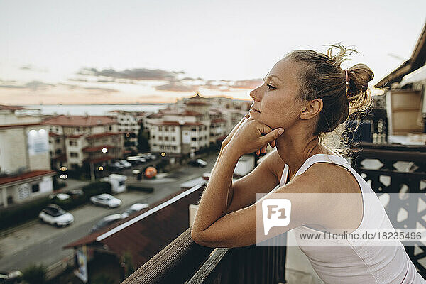 Woman leaning on railing of roof terrace at sunset looking at view