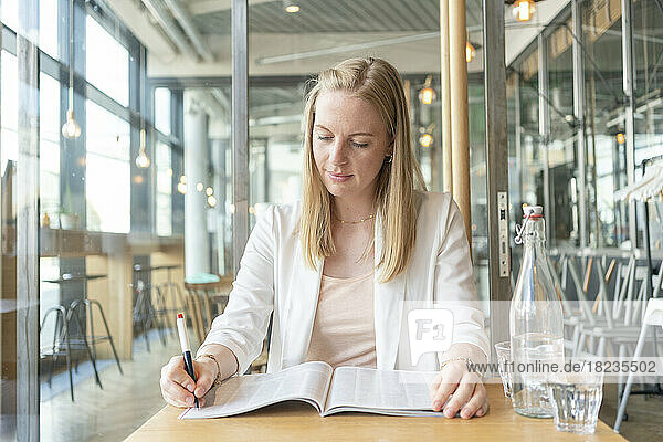 Young businesswoman marking in magazine with pen at cafe