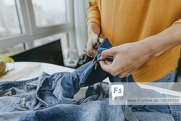 Hände eines jungen Modedesigners  der in der Werkstatt Jeans mit einer Schere schneidet