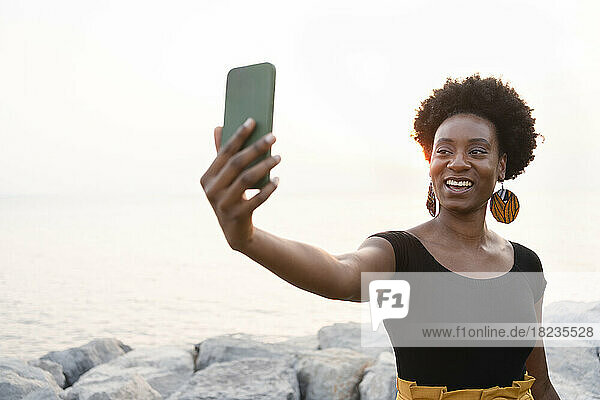 Happy woman taking selfie through mobile phone at sunset