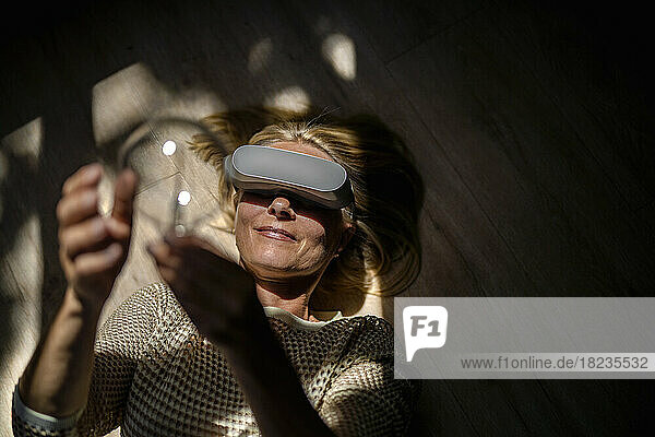 Smiling mature woman with light bulb wearing virtual reality glasses at home