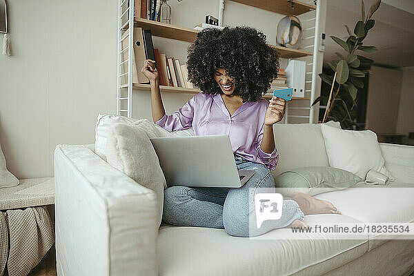 Glückliche Frau mit Kreditkarte beim Online-Shopping am Laptop zu Hause