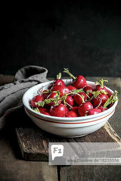 Fresh radishes in bowl at table