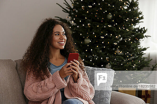 Happy young woman sitting with smart phone at home