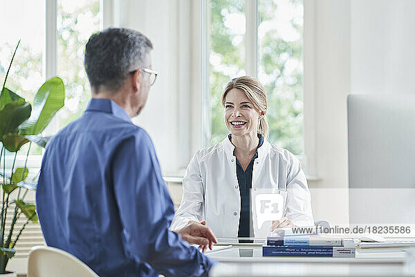 Happy female doctor sitting at desk with patient in medical practice