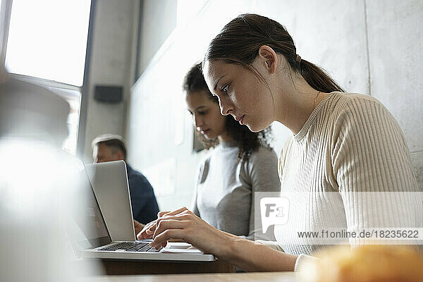 Businesswoman using laptop working by colleague at cafe