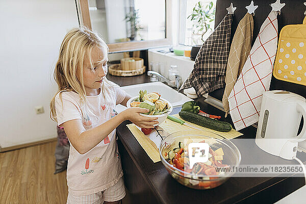 Girl collecting organic waste from vegetables in kitchen