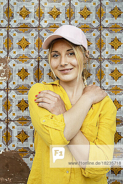 Young woman wearing cap standing in front of patterned wall