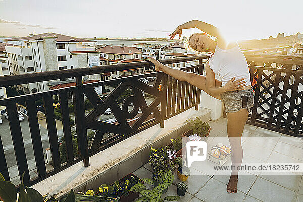 Woman doing stretching exercise on roof terrace at sunset