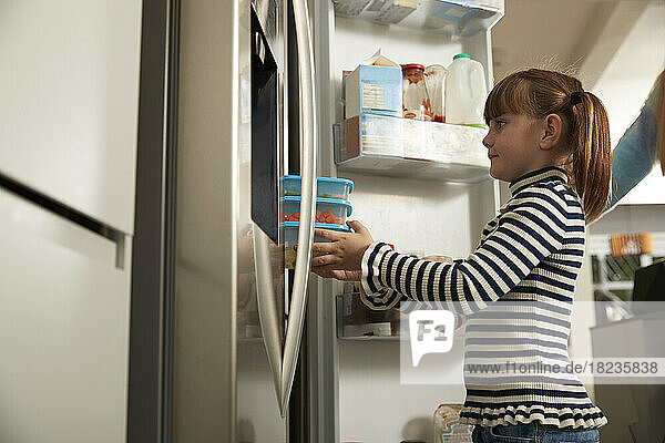 Mädchen hält zu Hause Plastikbehälter im Kühlschrank