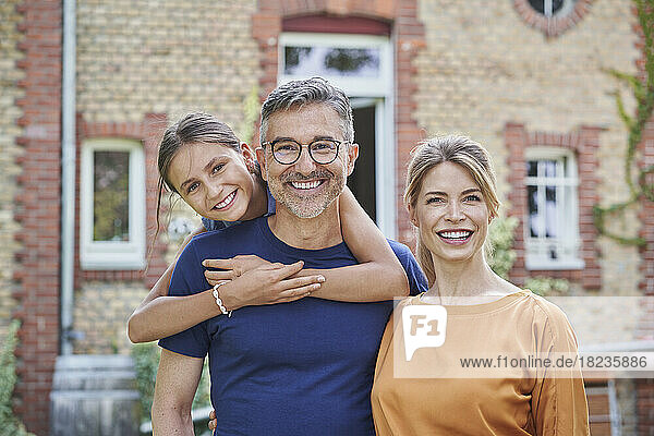 Smiling girl with father and mother in front of house