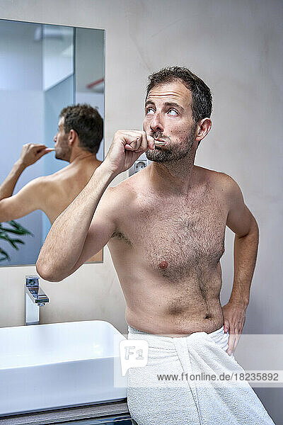 Man brushing teeth leaning on bathroom sink at home