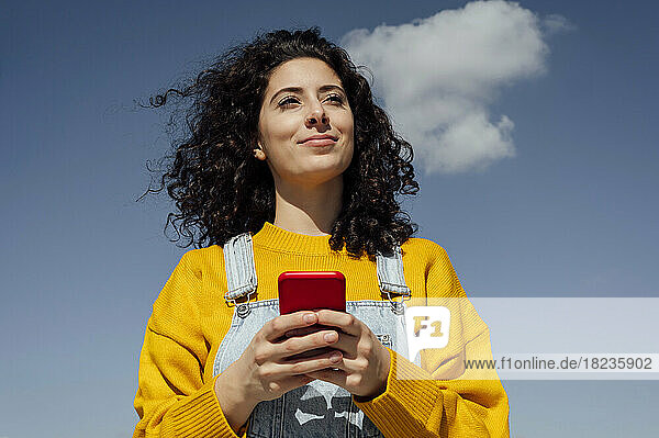 Thoughtful woman holding mobile phone under sky