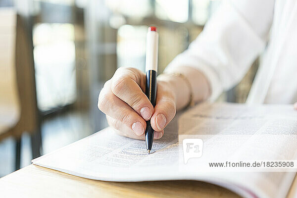 Hand of businesswoman marking in magazine with pen at cafe