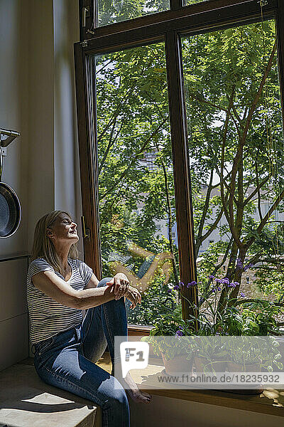 Woman sitting with eyes closed near window at home
