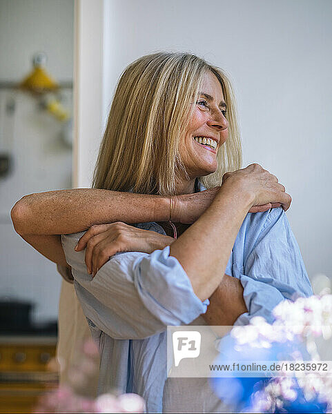 Happy woman with friend hugging from behind at home
