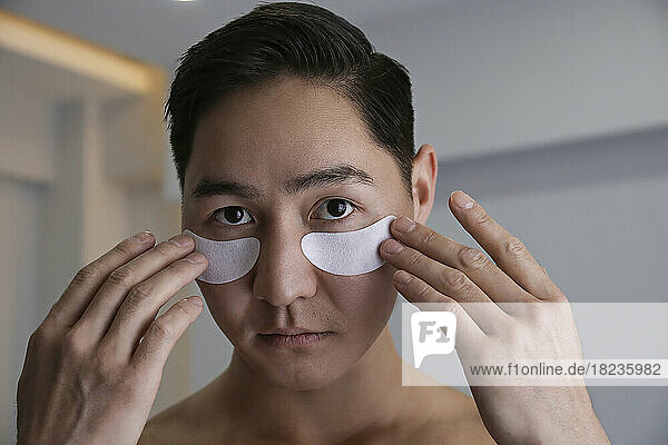 Young man applying under eye mask at home