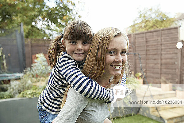 Smiling girl giving piggyback ride to sister in garden