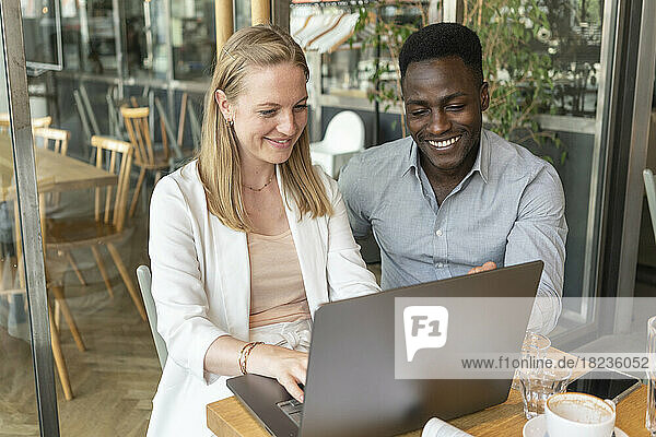 Glückliche Geschäftsfrau  die mit einem Kollegen im Café am Laptop arbeitet