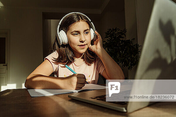 Girl wearing wireless headphones studying on laptop at desk