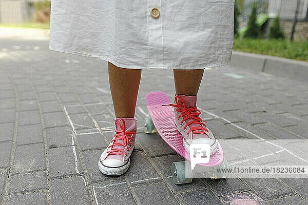 Mädchen mit rosa Skateboard steht auf Fußweg