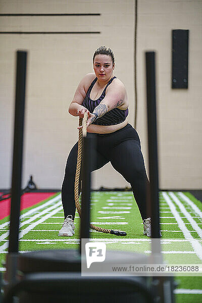 Overweight woman pulling weights with rope in gym