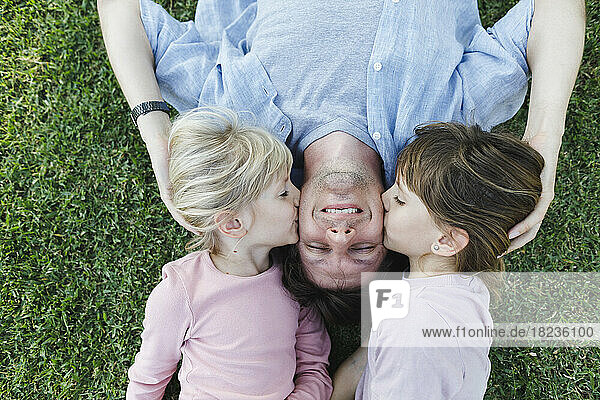 Töchter küssen ihren Vater auf die Wangen und entspannen sich im Gras