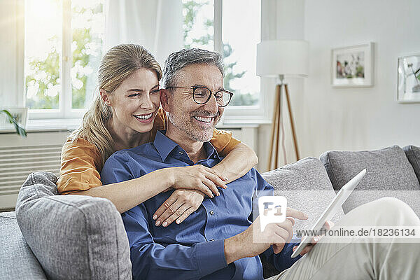 Happy woman embracing man using tablet PC on sofa at home