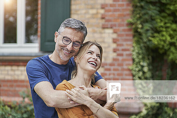 Smiling man embracing happy woman in front of house