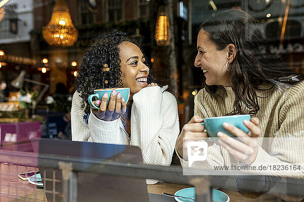 Glückliche Frau spricht mit einer Freundin  die im Café eine Tasse hält