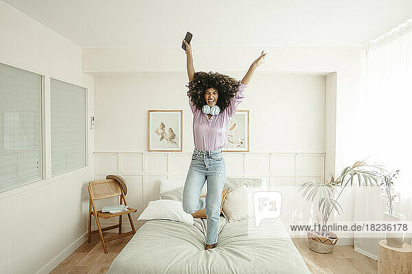 Happy woman with arms raised dancing on bed in bedroom