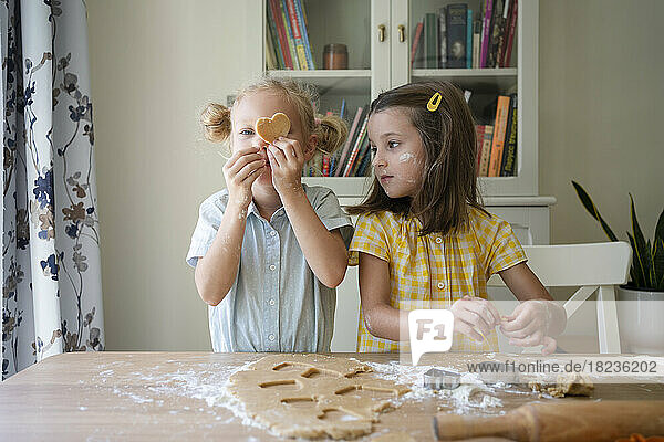 Girls preparing cookie with dough on table at home