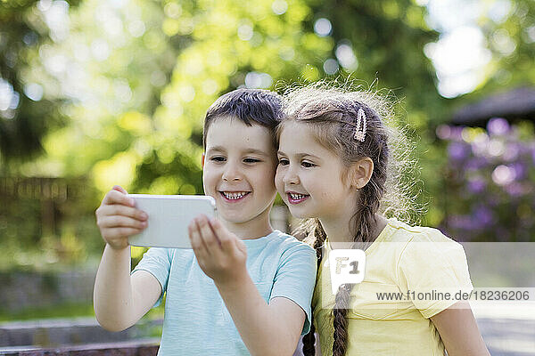 Smiling brother and sister using smart phone in back yard