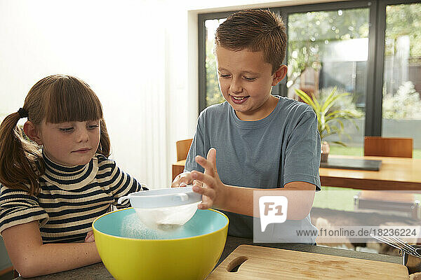 Smiling boy sieving flour by sister at home