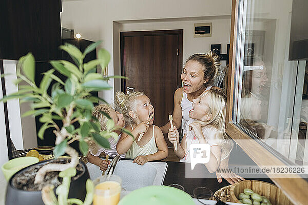 Mother watching daughters brushing their teeth with wooden brushes in the kitchen