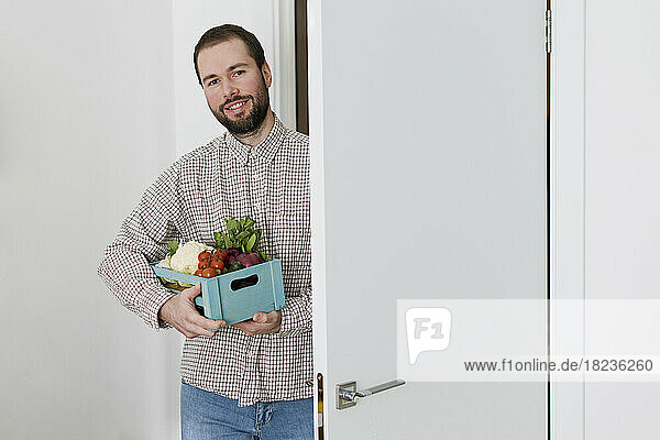 Lächelnder Mann mit einer Kiste frischem Gemüse steht vor der Tür