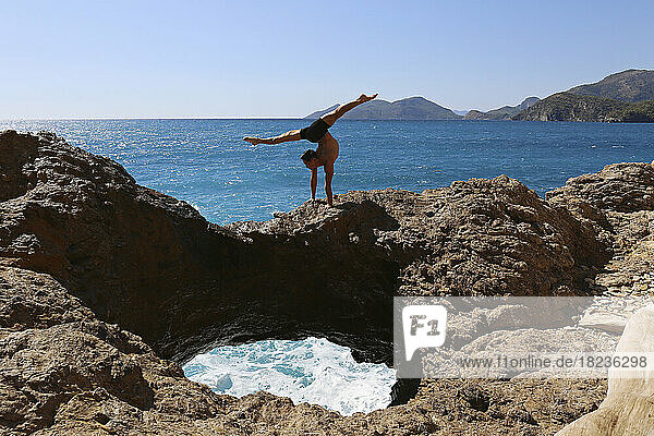 Athlete doing gymnastics on rock by sea