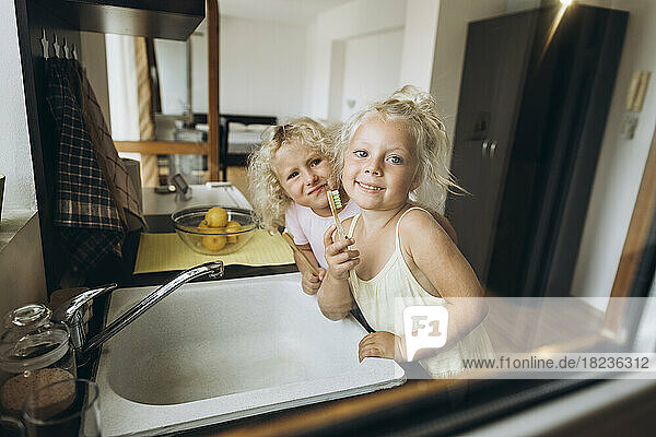 Smiling girls showing wooden toothbrushes in the kitchen