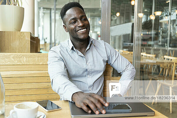 Happy businessman sitting with laptop and smart phone in cafe